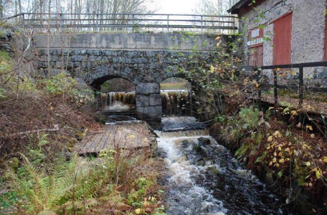 Äldre byggnad och en bro med vatten som forsar från en damm