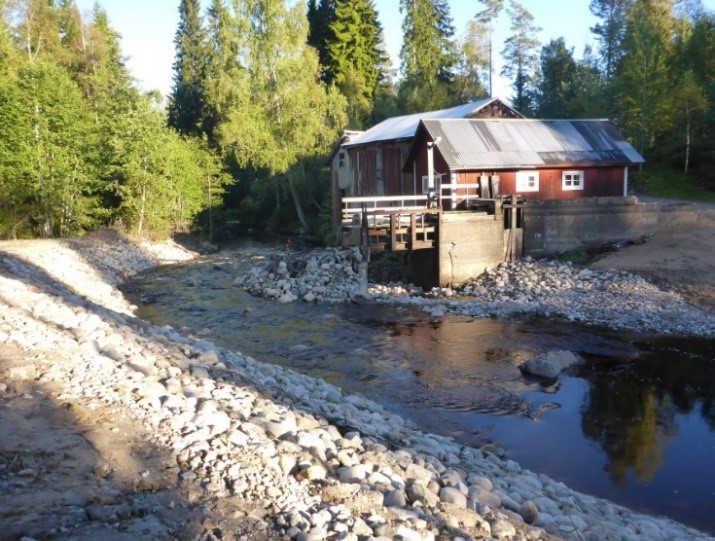 Forsande vatten med en vall till vänster och en röd byggnad i bakgrunden.