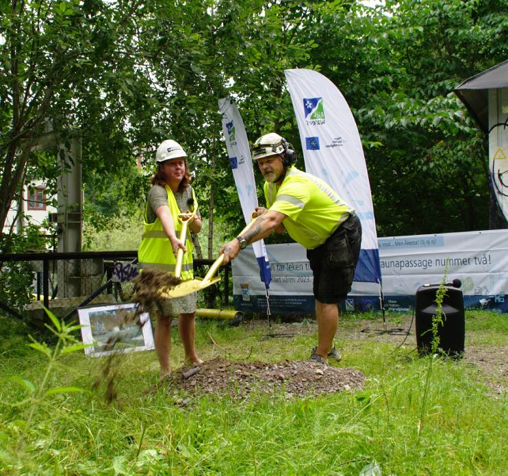 En kvinna och en man i gula varselkläder skottar med varsin spade