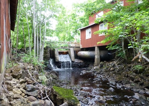 Röd byggnad med fördämning, där vatten rinner ned i ett vattendrag