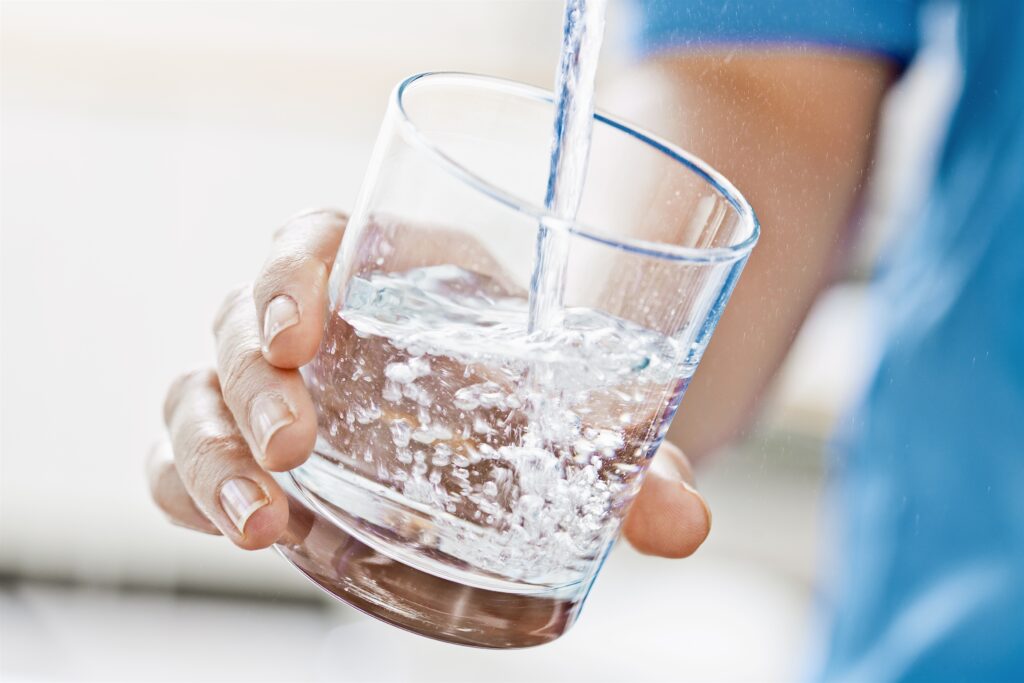 En hand håller i ett dricksvattenglas som fylls på med vatten från en kran.