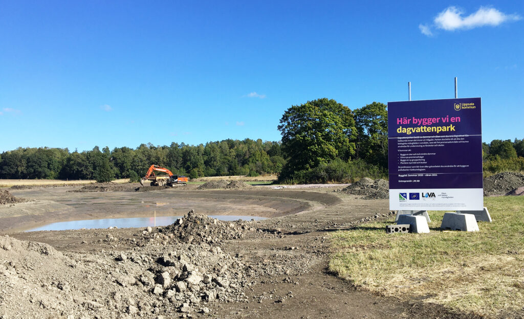 Grävarbeten vid platsen för vattenparken, med en informationsskylt i förgrunden.