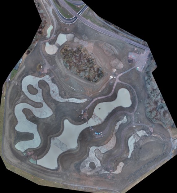 Bilden visar ett flygfoto över ett fält med skogspartier. På fältet syns flera dammar fyllda med vatten.