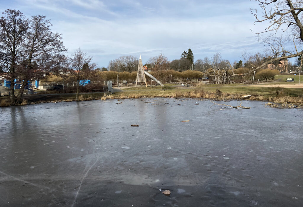 Isbetäckt damm med lekpark i bakgrunden.