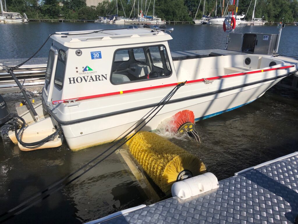 En vit båt som får botten rengjord av en gul och en röd borste.