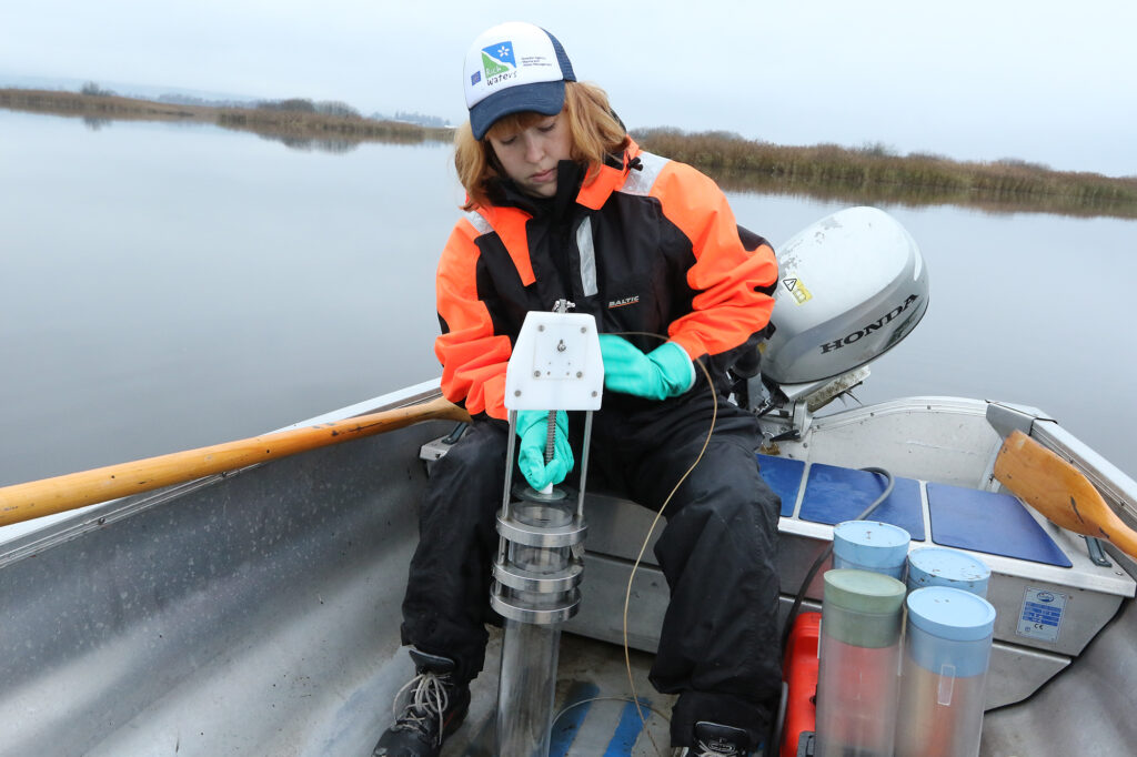 En bild som visar en kvinna i en båt som använder en utrustning för att ta prover från sjöns sediment.