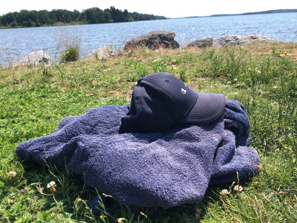 En blå badrock en blå keps ligger på en gräsmatta vid en sjö.
