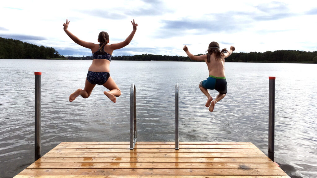 Två barn i badkläder som hoppar från en badbrygga.