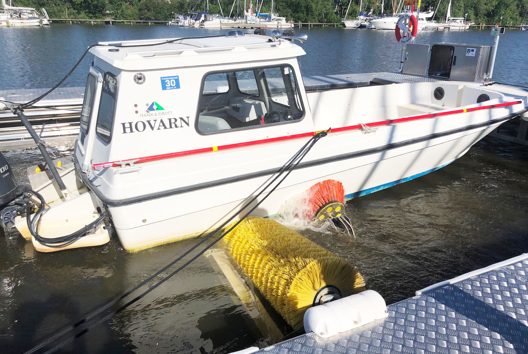 En båtbottentvätt där en vit båt får sin botten tvättad av en stor gul borste.