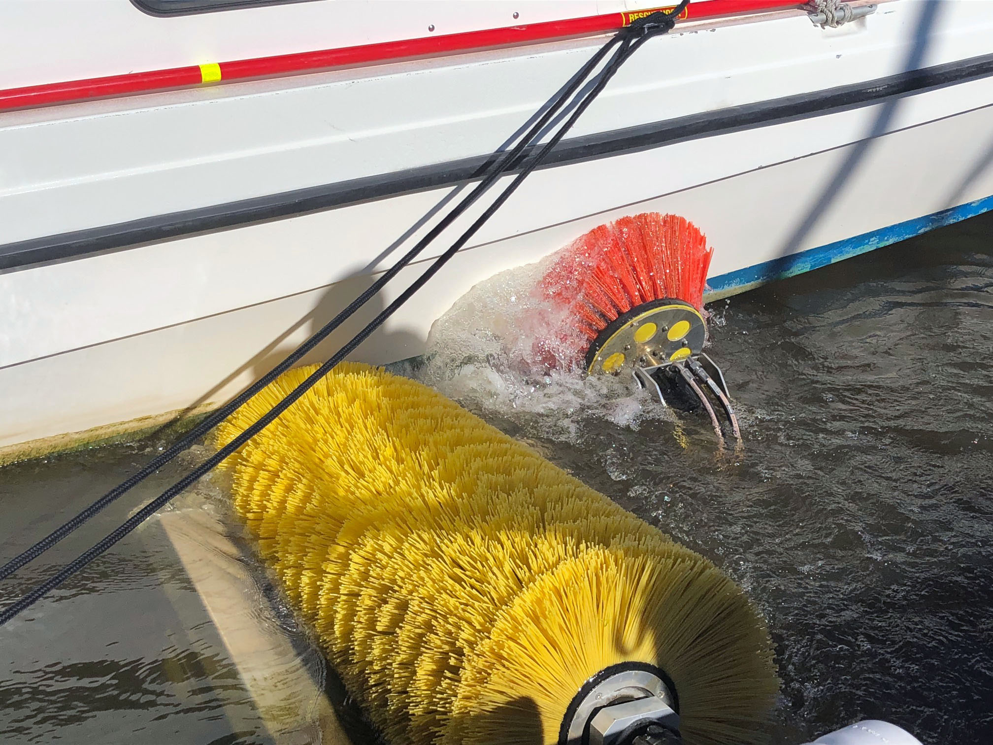 En stor gul borste och en mindre röd borste, tvättar underredet på en båt.